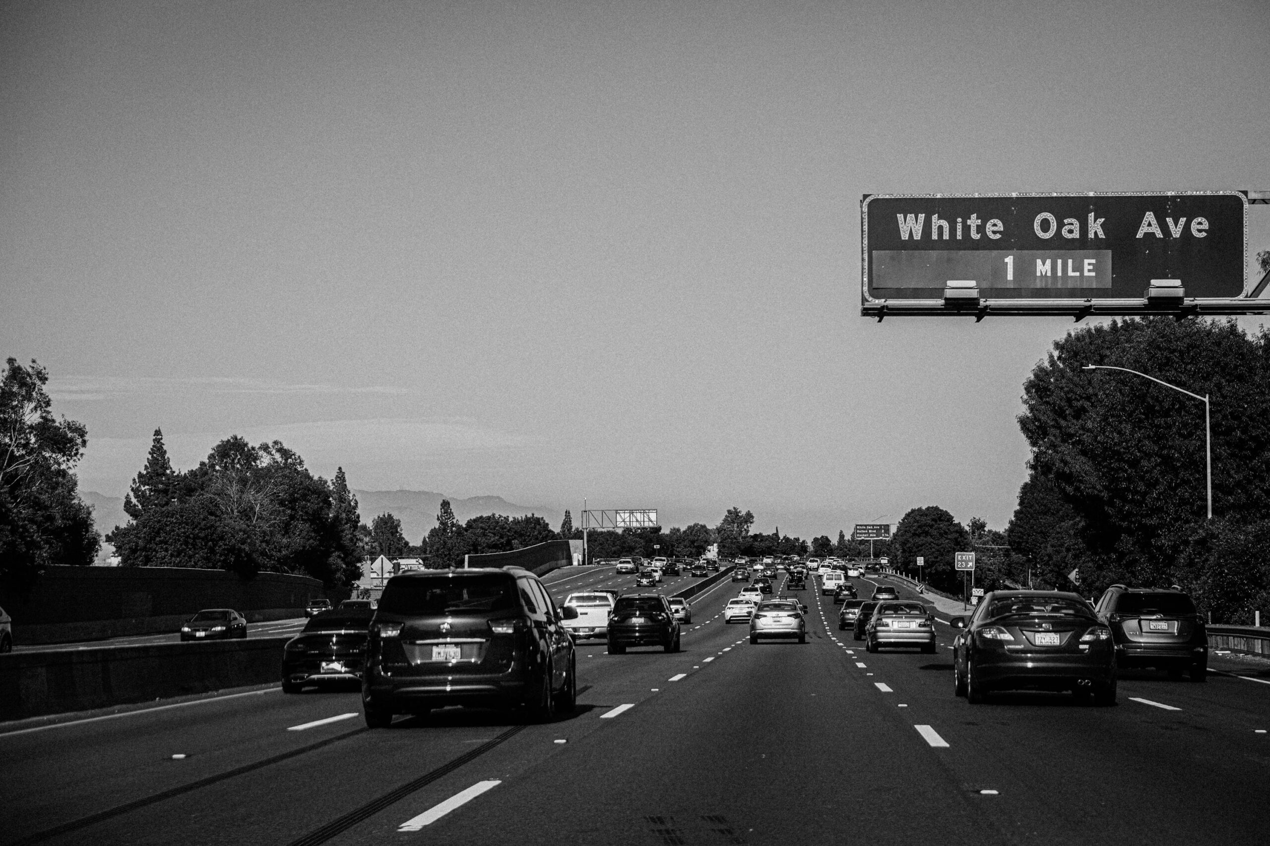 Busy Los Angeles highway scene in grayscale, featuring vehicles and road signs.